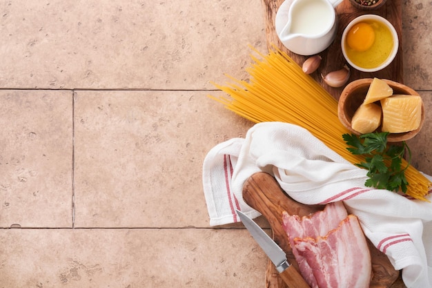 Ingredients for Pasta Carbonara Traidtional Italian Pasta Carbonara Ingredients bacon spaghetti parmesan and egg yolk garlic Beige old tile table background Top view Copy space