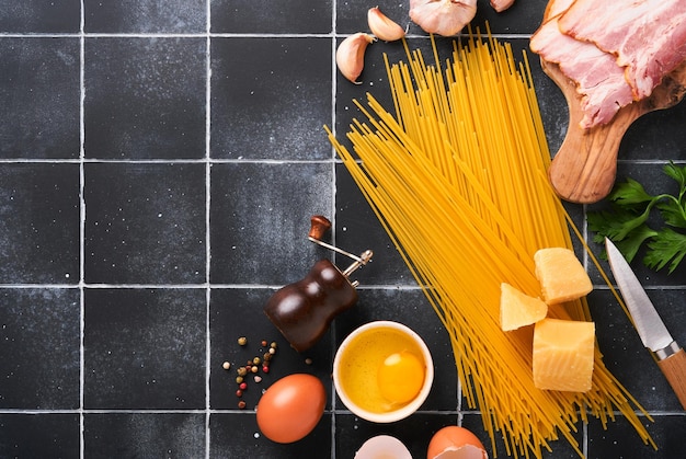 Ingredients for Pasta Carbonara Traidtional Italian Pasta Carbonara Ingredients bacon spaghetti parmesan and egg yolk garlic Black old tile table background Top view Copy space