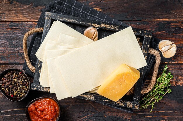 Ingredients for the preparation of Lasagna, Tomatoes, sauce, pasta. Dark wooden background. Top view.