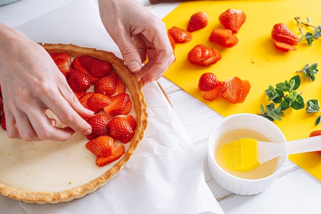 Ingredients for strawberry pie custard cake with lime zest cutting board with sliced strawberries female hands lay sliced strawberries on the surface of the cream