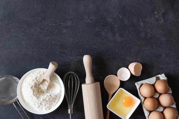 Ingredients and tools for dough preparation on black background top view Baking background