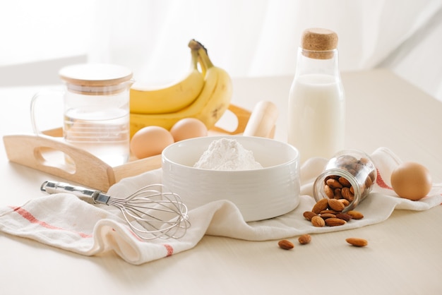 Ingredients and tools to make banana cake on white surface