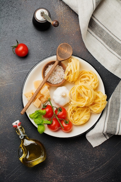 Ingredients for traditional Italian pasta dish. Uncooked raw tagliatelle bolognesi, parmesan cheese, olive oil, garlic, basil leaves, pepper, cherry tomatoes. Top view