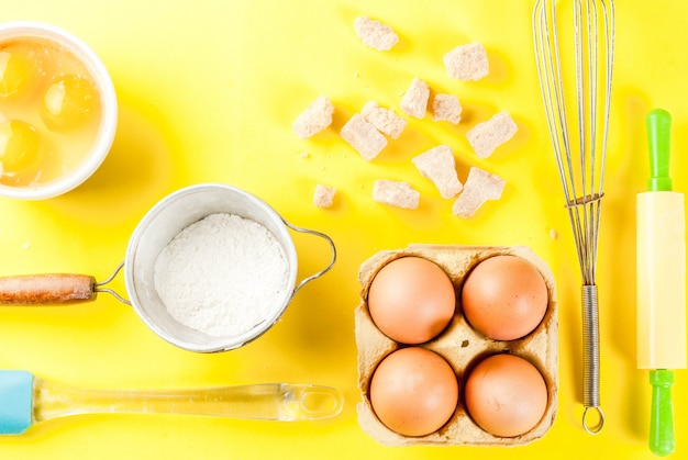 Ingredients and utensils for cooking baking egg, flour, sugar, whisk, rolling pin, on bright yellow background, top view