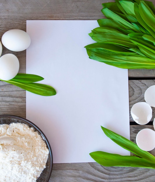 Ingredients for wild garlic pies and a white sheet for writing down the recipe Wooden background