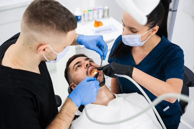 Photo initial examination of the patients oral cavity by dentist handsome man is having preventive dental checkup in clinic