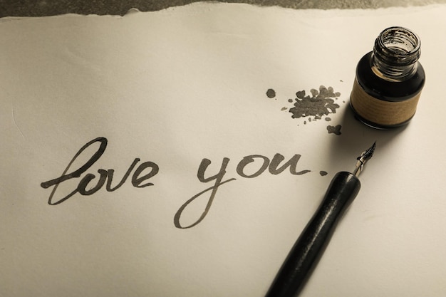 Photo ink bottle pen and words love you on paper on gray background close up