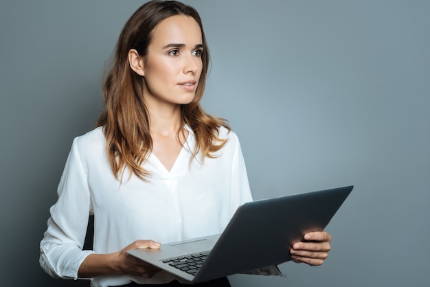 Innovative device. Nice pleasant good looking woman holding her laptop and looking in front of her while being distracted from work