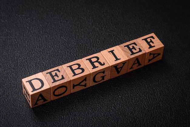 Photo the inscription debrief in wooden cubes on a dark concrete background