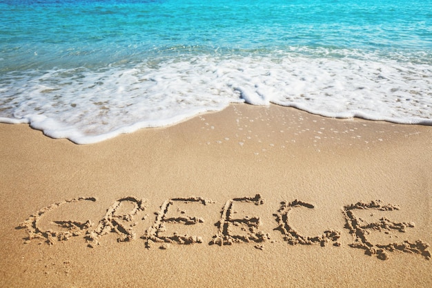 Inscription GREECE on a sandy beach with sea waves Nature background