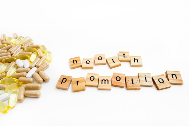 Inscription HEALTH PROMOTION in wooden cubes on a white background of different pills