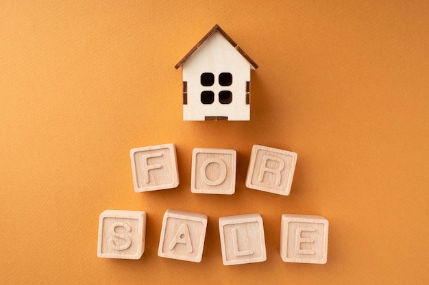 The inscription house for sale made of wooden cubes on an orange background The concept of selling a house or apartment Layout of a wooden house