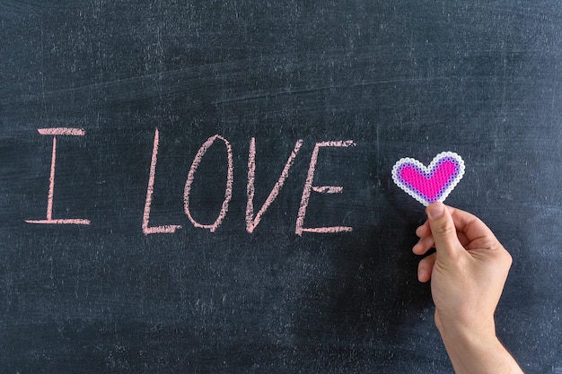 The inscription "I LOVE" on the chalk board. Hand with heart symbol