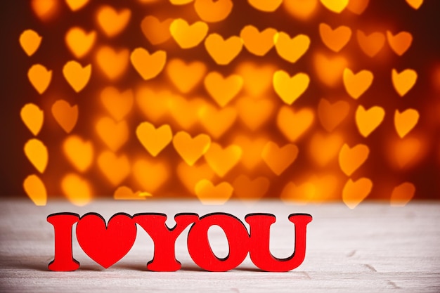 The inscription I Love You on a wooden background with beautiful hearts made of lights on a blurred background