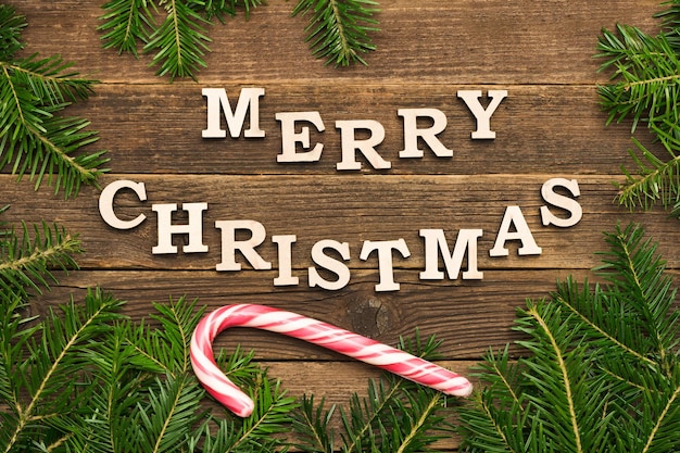 Inscription Merry Christmas on a wooden background Frame of fir branches lollipop stick