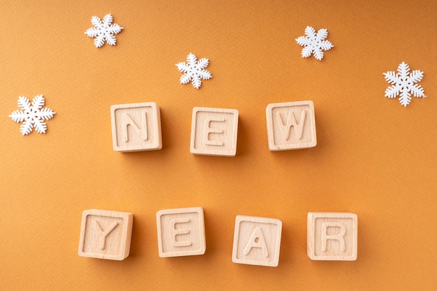 The inscription new year on wooden cubes Wooden cubes with letters and snowflakes on an orange background New Year's card