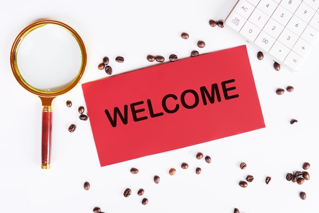 The inscription welcome on a red card on a white background next to coffee beans and a magnifying glass