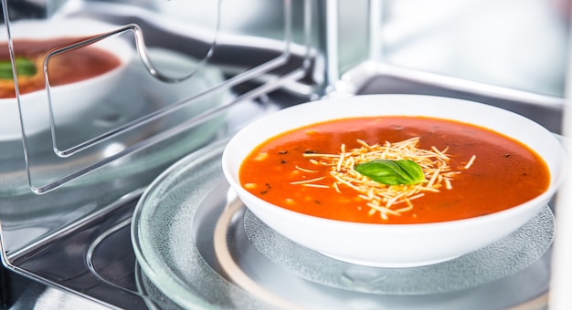 Inside view of new clean staniless microwave oven with a tomato soup in white plate.