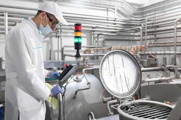 Inspector in a mask and a scrub stands with a foldertablet in his hands at the dairy plant