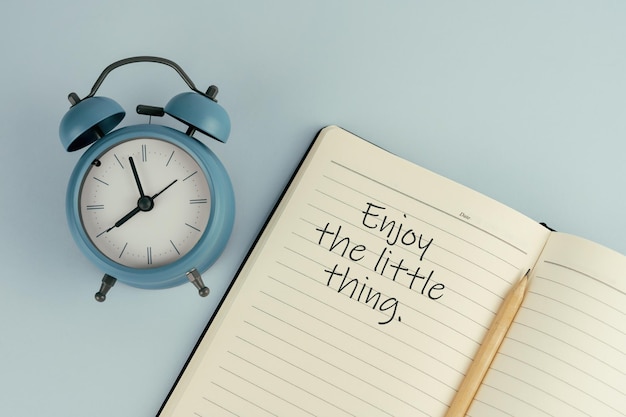 Inspirational quote Enjoy the little thing text on note pad with alarm clock