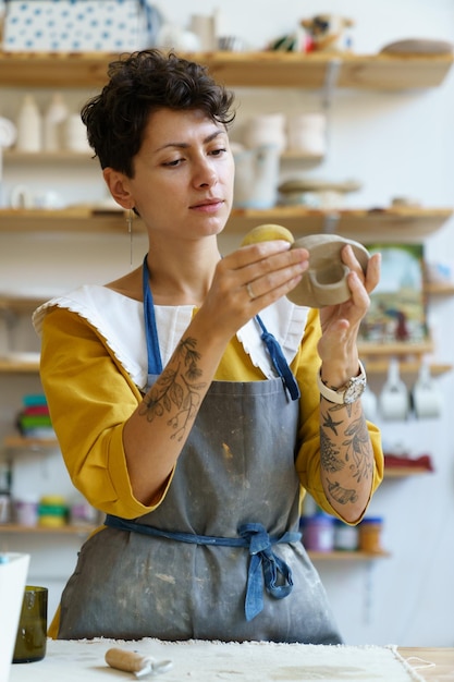 Inspired woman using sponge to absorb water on clay kitchenware visiting ceramics workshop