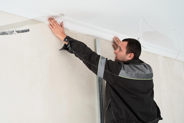 Installation of ceiling detail moldings Worker fixes the plastic molding to the ceiling