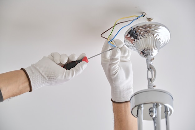 Installation ceiling lamp, hands of male electrician fixing chandelier with use of professional tools