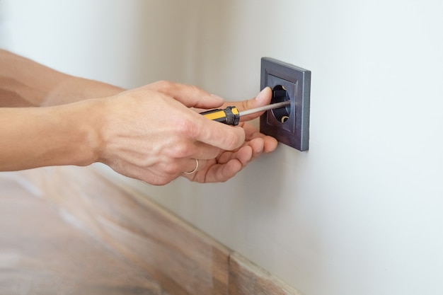 Installation of electrical sockets in closeup of hand of electrician installing wall outlet.