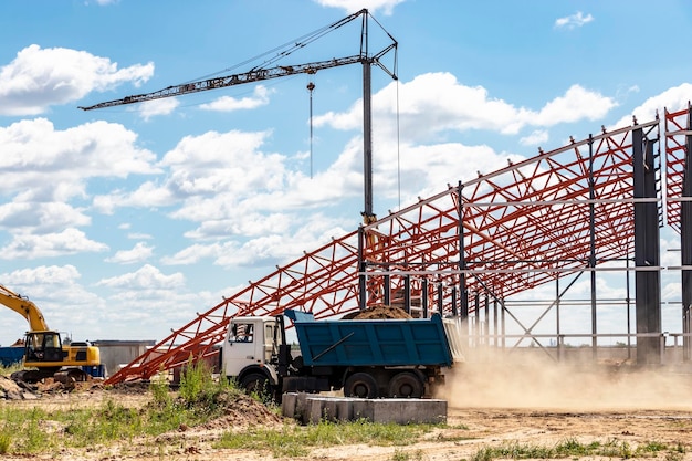 Installation of metal trusses and frame during the construction of an industrial building or factory The dump truck removes excess soil from the construction site Construction of a large frame shop