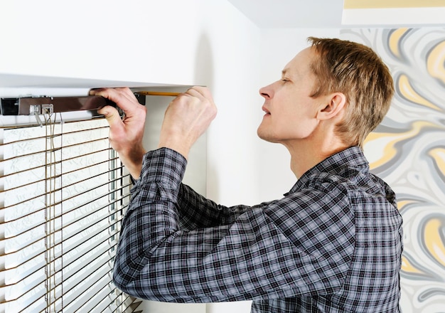 Installing wooden blinds. Man marks the place of mounting jalousie on the windows.