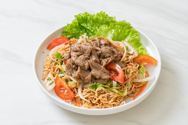 instant noodle spicy salad with pork on white plate - Asian food style