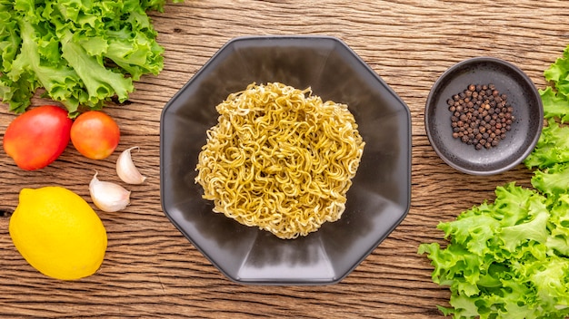 Instant noodle with pepper, lettuce, tomato, garlic and lemon on rustic natural wood background