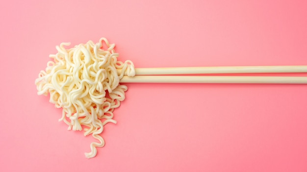 Instant noodles and chopsticks on pink 