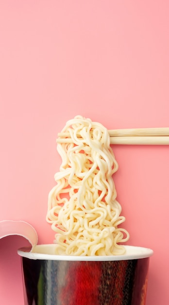 Instant noodles cup and chopsticks on pink 