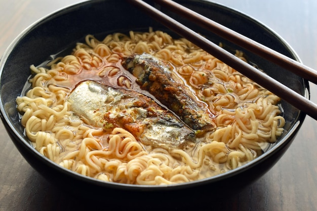 Instant noodles soup with sardine and seasoning in a black bowl