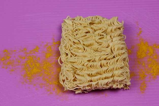 Instant noodles with spices on a purple background Fast food concept idea Closeup View from above