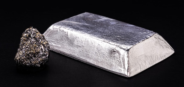 Insulated zinc ingot or bar next to raw zinc nugget on insulated black background, metal used in the production of alloys and steel