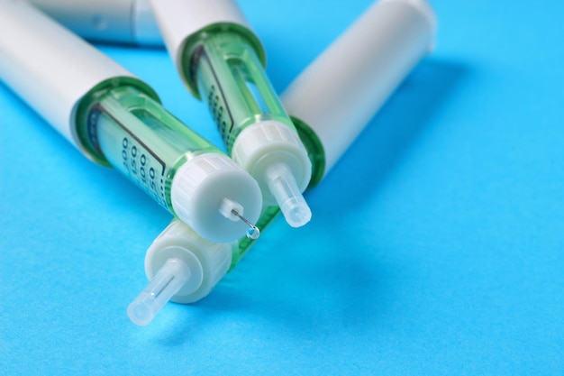 Insulin syringe pen with a drop of medicine at the end of the needle on a blue background