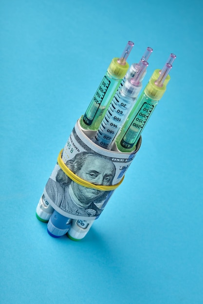 Insulin syringe pens wrapped in dollar bills on a blue background Inflation and raising drug prices