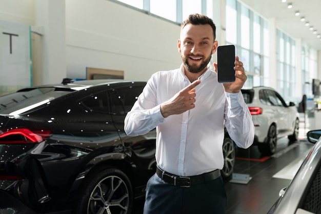 Insurance agent in the showroom of a car dealership demonstrates the screen of a smartphone