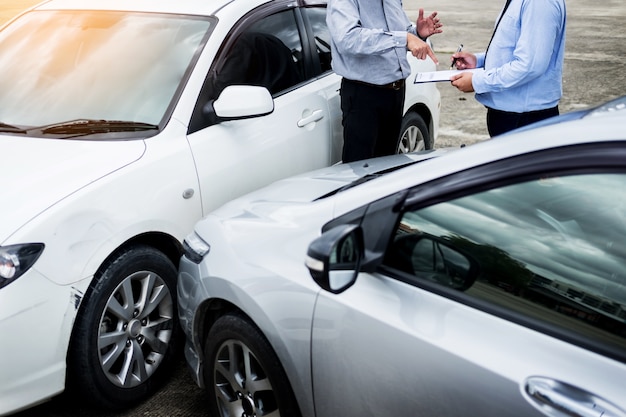 Insurance agent writing on clipboard while examining car after accident