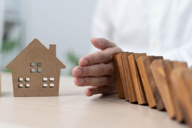 Insurance with hands protect a house The wooden domino block is about to fall on the house Home insurance or house insurance concept