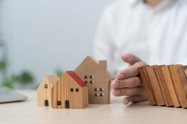 Insurance with hands protect a house The wooden domino block is about to fall on the house Home insurance or house insurance concept