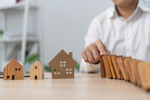 Insurance with hands protect a house The wooden domino block is about to fall on the house Home insurance or house insurance concept