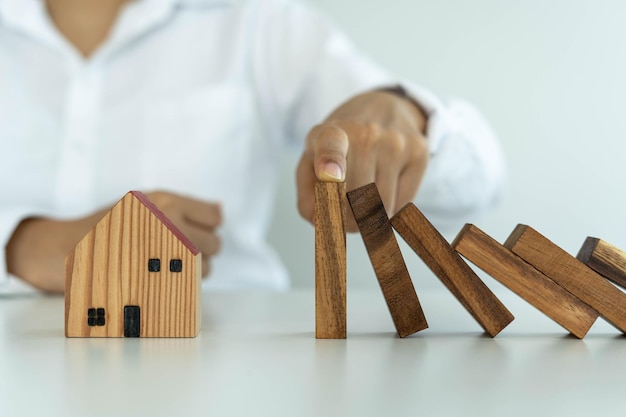 Insurance with hands protect a house The wooden domino block is about to fall on the house Home insurance or house insurance concept