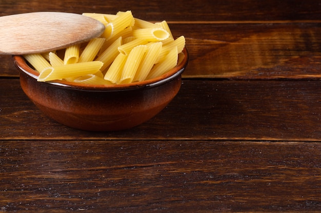 Integral Penne into a brown bowl with a wooden spoon over a wooden table