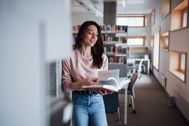 Intellectual growth. Brunette girl in casual clothes having good time in the library full of books