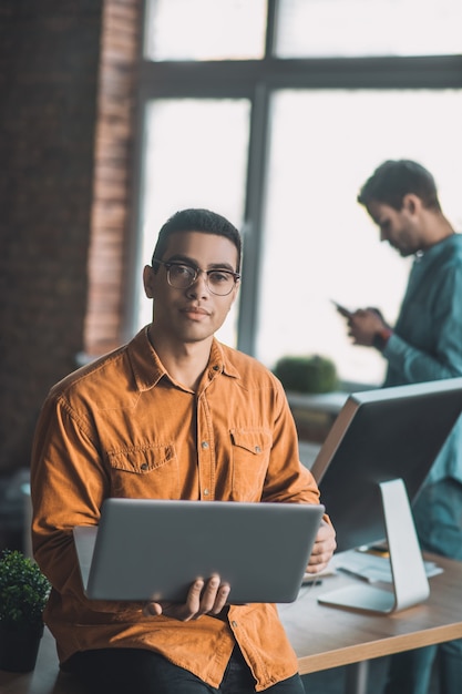 Intelligent handsome man wearing the eyeglasses while having his laptop in his hands