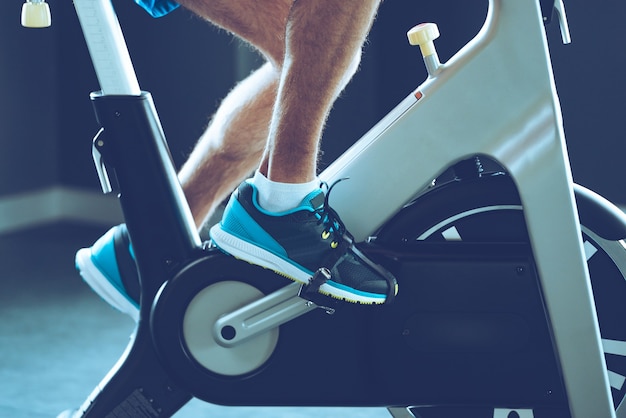 Intense cardio workout. Side view close-up part of young man in sports shoes cycling at gym