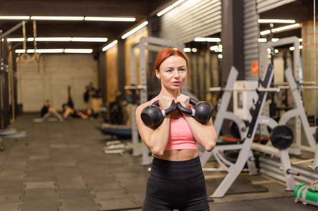 Intensive workout redhaired woman with kettlebells in her hand in modern gym